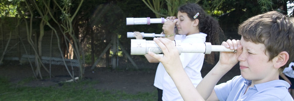 Three children peering through homemade telescopes