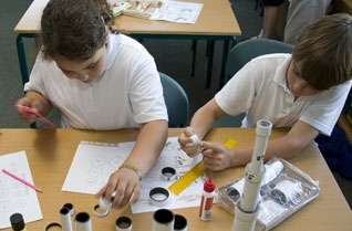 Boy and a girl building a cardboard tube telescope in a classroom