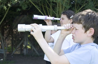 Children looking through cardboard tube telescopes outside