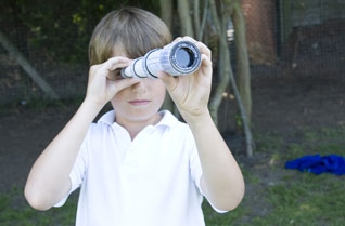 Young boy looking at the camera through a cardboard tube telescope