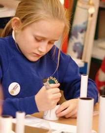 Young girl making a cardboard tube telescope in a classroom