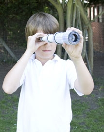 Young boy looking through a cardboard tube telescope outside