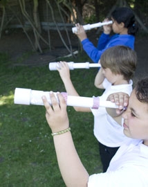 Three children looking through cardboard tube telescopes outside