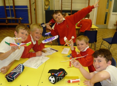 5 lively children around a table about to launch aeroplanes